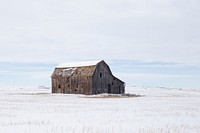 A rustic farm shed sitting in the middle of snow covered farm field under a cloudy sky. Original public domain image from Wikimedia Commons