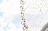 A white Ferris wheel with passenger cars painted with different faces on them in Paris. Original public domain image from Wikimedia Commons