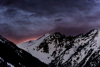 A snow-capped mountain ridge under dark gray evening sky. Original public domain image from Wikimedia Commons