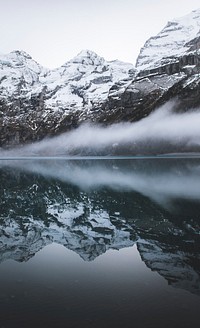 Reflections of snowy mountains reflect in calm foggy waters of Oeschinen Lake. Original public domain image from Wikimedia Commons