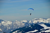 Person parachutes over mountains in a blue landscape. Original public domain image from <a href="https://commons.wikimedia.org/wiki/File:Parapente_(Unsplash).jpg" target="_blank" rel="noopener noreferrer nofollow">Wikimedia Commons</a>