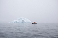 A group of people in a raft in the middle of the ocean next to a small iceberg with fog surrounding the area.. Original public domain image from <a href="https://commons.wikimedia.org/wiki/File:Zodiac_passing_by_a_small_piece_of_an_iceberg_(Unsplash).jpg" target="_blank" rel="noopener noreferrer nofollow">Wikimedia Commons</a>