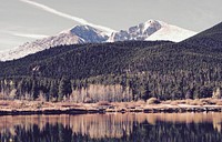 A long mountain ridge behind wooded hills near a lake in Estes Park. Original public domain image from Wikimedia Commons