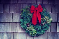A Christmas wreath with a red bow and pinecones hanging on the side of a shingled house. Original public domain image from Wikimedia Commons