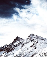 A mountain peak in the snow with a dramatic cloudy sky. Original public domain image from Wikimedia Commons