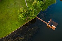 A drone shot of a boathouse on a lake near a green park. Original public domain image from Wikimedia Commons