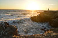 Man standing on a cliff by the ocean bay looking at the sunset at Leo Carrillo State Beach. Original public domain image from Wikimedia Commons