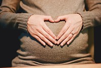 A pregnant woman in a sweater forming a heart with her hands on her belly. Original public domain image from Wikimedia Commons