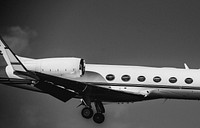 Cropped black and white photo of private jet in mid-flight.. Original public domain image from <a href="https://commons.wikimedia.org/wiki/File:Close_up_landing_(Unsplash).jpg" target="_blank" rel="noopener noreferrer nofollow">Wikimedia Commons</a>