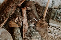 A broom leaning against a wall next to a disorderly heap of firewood. Original public domain image from Wikimedia Commons