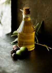 A glass jug of extra virgin olive oil next to some fruit on a table. Original public domain image from <a href="https://commons.wikimedia.org/wiki/File:Olive_Oil_(Unsplash).jpg" target="_blank" rel="noopener noreferrer nofollow">Wikimedia Commons</a>