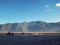 A plain at the foot of a mountain range with people on horseback and on foot. Original public domain image from <a href="https://commons.wikimedia.org/wiki/File:Riding_lessons_in_the_mountains_(Unsplash).jpg" target="_blank" rel="noopener noreferrer nofollow">Wikimedia Commons</a>
