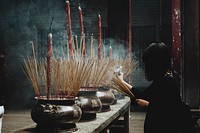 A woman places joss sticks in urns with joss sticks of various sizes in the temple.. Original public domain image from Wikimedia Commons