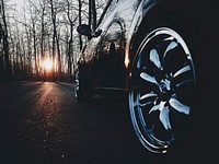 Black car chrome rim on an asphalt road in a leafless forest on sunset. Original public domain image from Wikimedia Commons