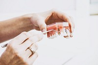 A dentist holding a fake set of teeth in her hands showing how implants work. Original public domain image from <a href="https://commons.wikimedia.org/wiki/File:Dental_implants_(Unsplash).jpg" target="_blank" rel="noopener noreferrer nofollow">Wikimedia Commons</a>