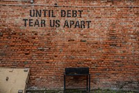 Graffiti on an old brick wall reads “until debt tear us apart”. Original public domain image from <a href="https://commons.wikimedia.org/wiki/File:Until_debt_tear_us_apart_(Unsplash).jpg" target="_blank" rel="noopener noreferrer nofollow">Wikimedia Commons</a>
