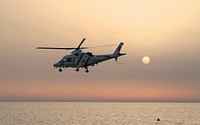 A helicopter flying over the water during sunset.. Original public domain image from Wikimedia Commons