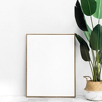 Blank gold photo frame by the houseplant on a floor