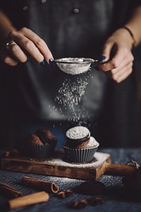 Woman sprinkling powdered sugar to cupcakes