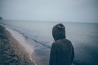 Person in a hoodie on a sandy beach filled with footprints. Original public domain image from Wikimedia Commons