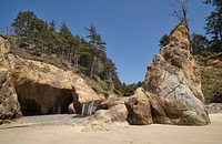 Coves at Hug Point State Recreation Site, a state park south of the seaside town of Cannon Beach on the northern coastline of the U.S. state of Oregon.  Erosion has formed caves in sandstone cliffs along the headland's south side, which is also the site of small, seasonal waterfalls (center). The Oregon Coast Trail passes though the park along the beach.