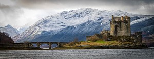 A castle on an island in Scotland with a bridge and a mountain in the background. Original public domain image from <a href="https://commons.wikimedia.org/wiki/File:Eilean_Donan_Castle_on_a_cloudy_day_(Unsplash).jpg" target="_blank" rel="noopener noreferrer nofollow">Wikimedia Commons</a>