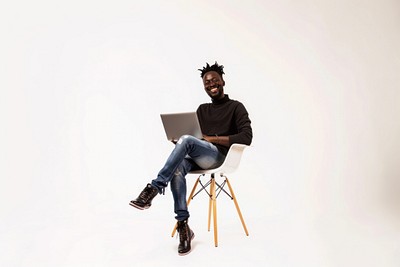 Black man smile to a camera with a laptop sitting background chair.