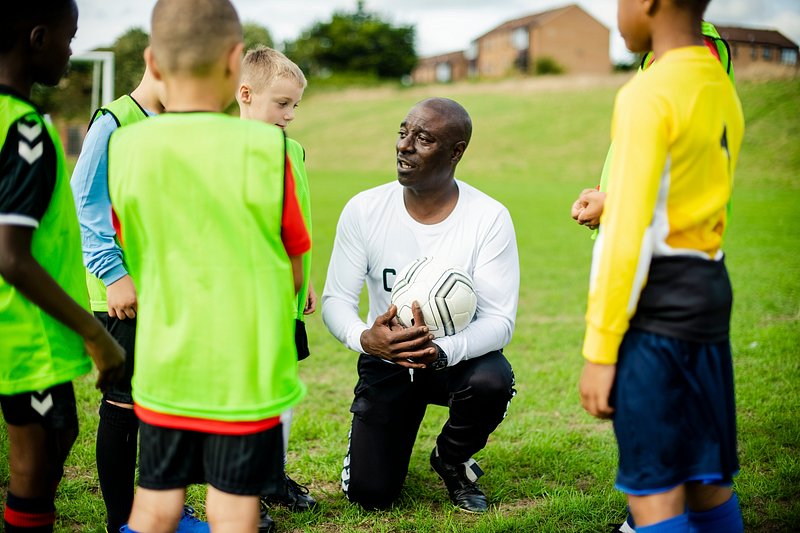 African American coach instructing diverse group of young soccer playing kids