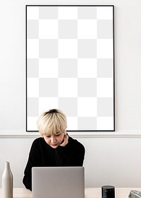 Asian woman working on her laptop with a blank frame hanging on a wall