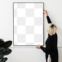 Blond haired Asian woman hanging a blank frame on a white wall