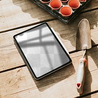 Png tablet screen mockup by a gardening trowel on a wooden table