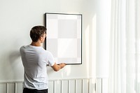 Transparent png frame being hung by a young man on a white minimal wall