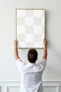 Transparent png frame being hung by a young man on a white minimal wall