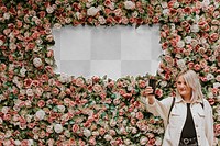 Sign mockup png with a woman taking a selfie by the flower wall installation