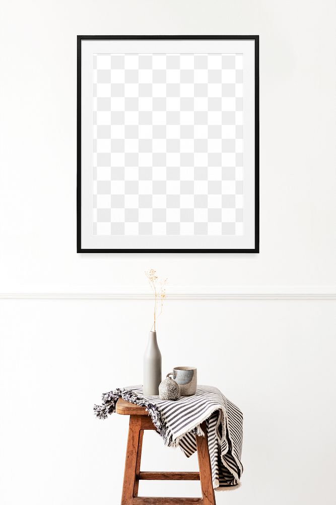 Picture frame mockup hanging on a white wall over a wooden stool with dried flowers 