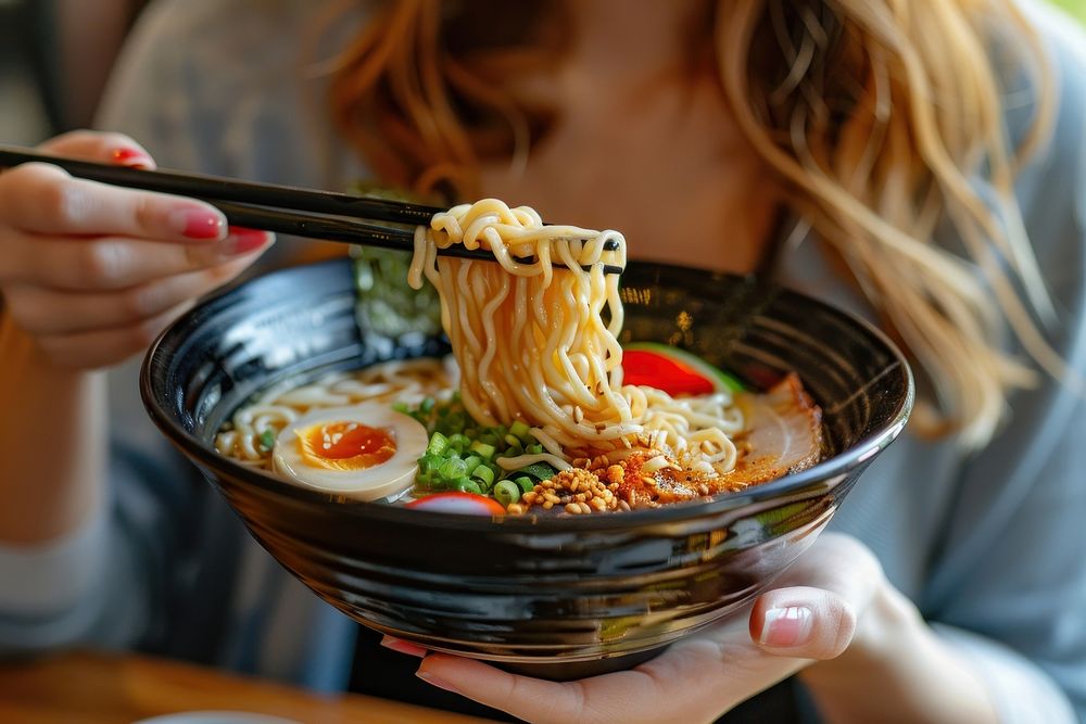 Cropped hand of asian woman eating a bowl of freshly served traditional Japanese ramen with chopsticks cutlery person human.