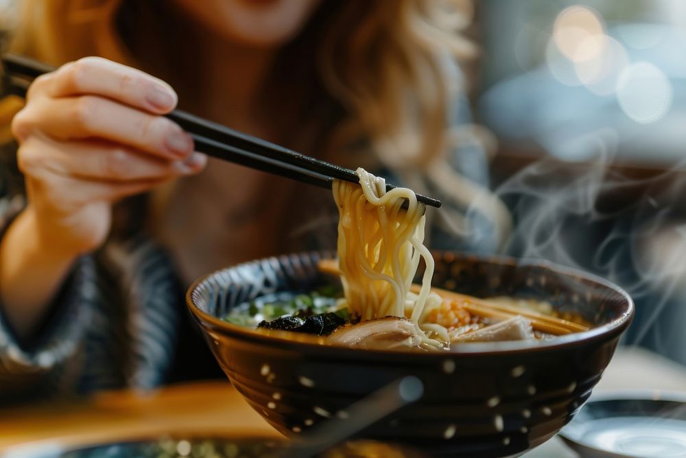 Cropped hand of asian woman eating a bowl of freshly served traditional Japanese ramen with chopsticks person human baton.