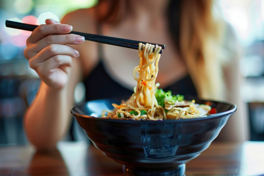 Cropped hand of asian woman eating a bowl of freshly served traditional Japanese ramen with chopsticks device brush food.