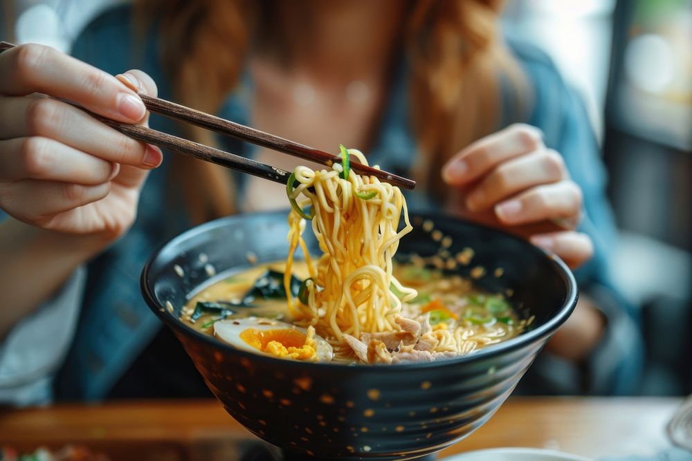 Cropped hand of asian woman eating a bowl of freshly served traditional Japanese ramen with chopsticks weaponry person…