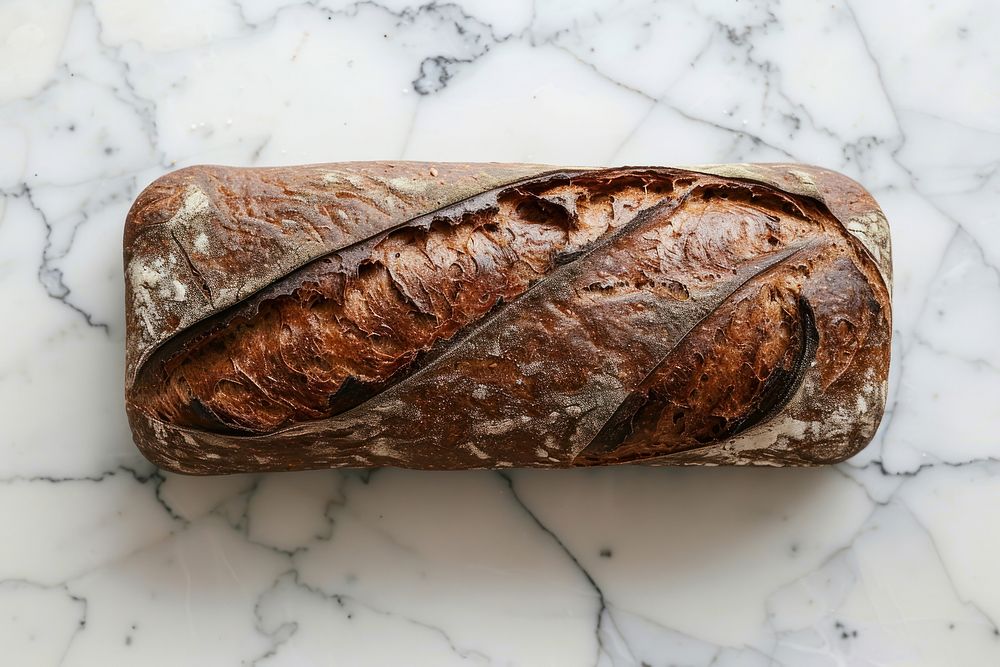 Photo of pumpernickle loaf of bread on light grey top baguette food.