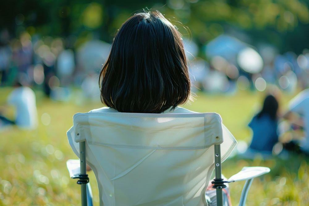 The back of woman sitting on empty white folding chair camping while seeing outdoor concert outdoors furniture female.