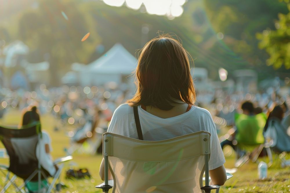 The back of woman sitting on empty white folding chair camping while seeing outdoor concert outdoors nature photography.