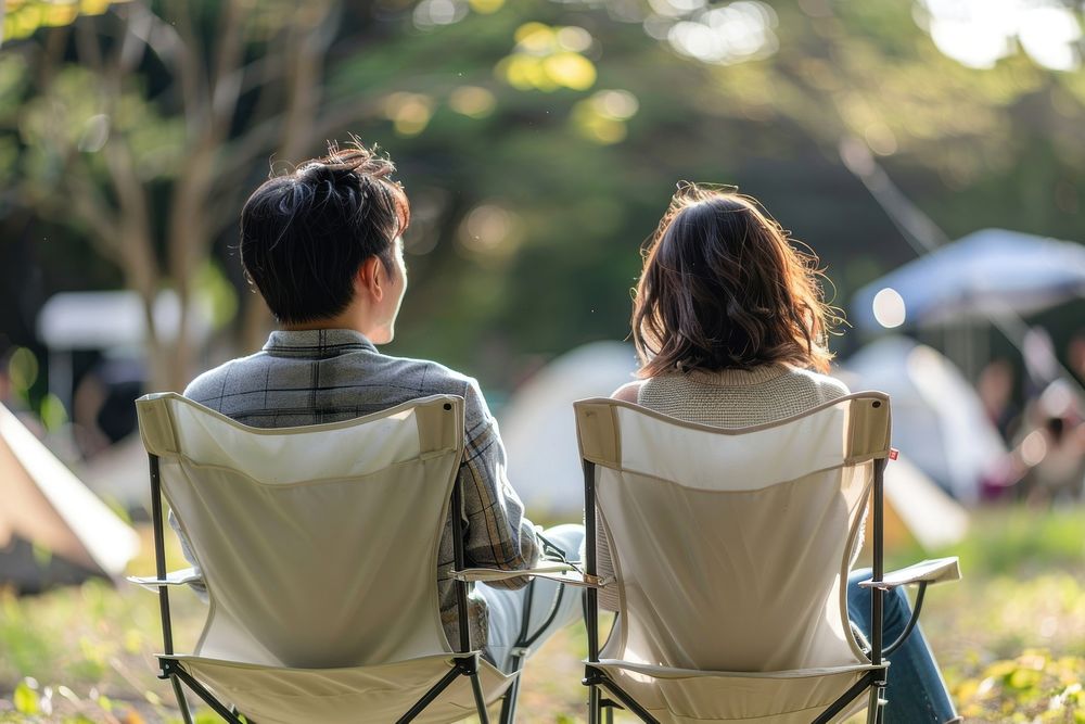 The back of couple sitting on empty white folding chair camping while seeing outdoor concert outdoors conversation furniture.