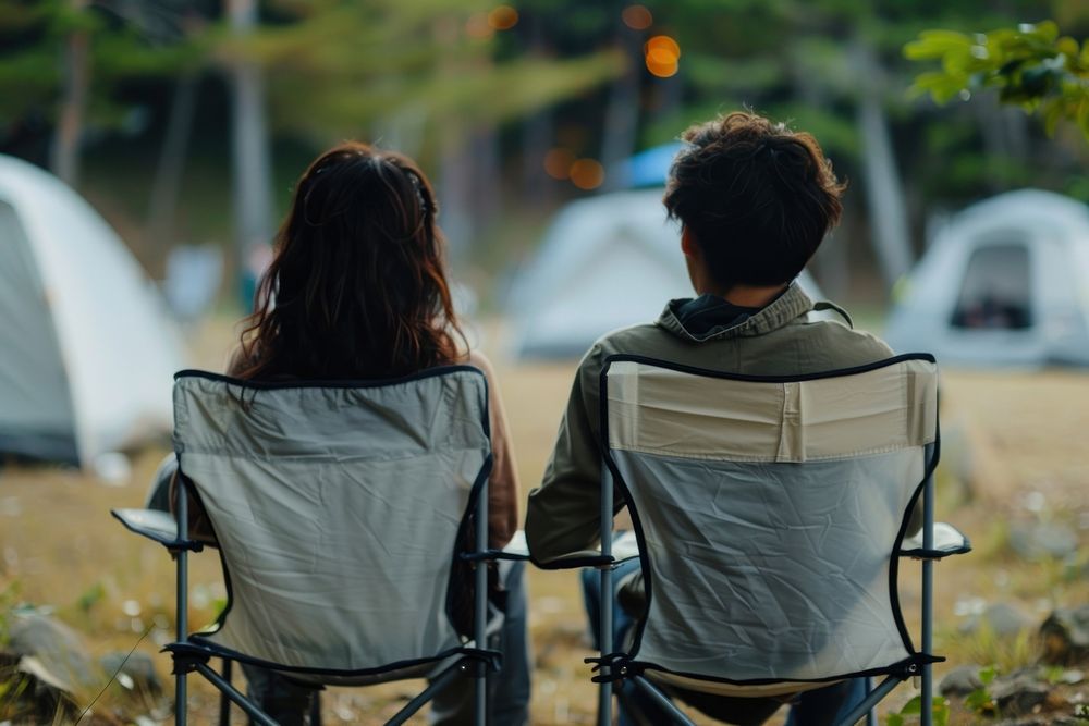 The back of couple sitting on empty white folding chair camping while seeing outdoor concert outdoors nature transportation.