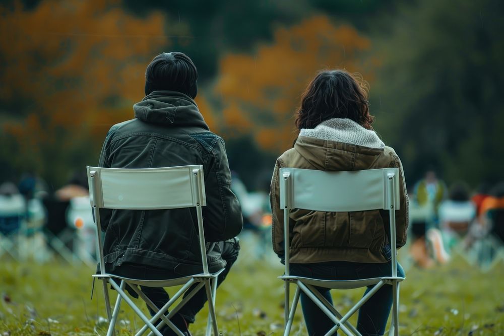 The back of couple sitting on empty white folding chair camping while seeing outdoor concert outdoors furniture walking.