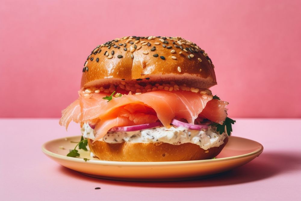 Bagel with creamcheese and salmon cut in half served on pink paper burger brunch bread.