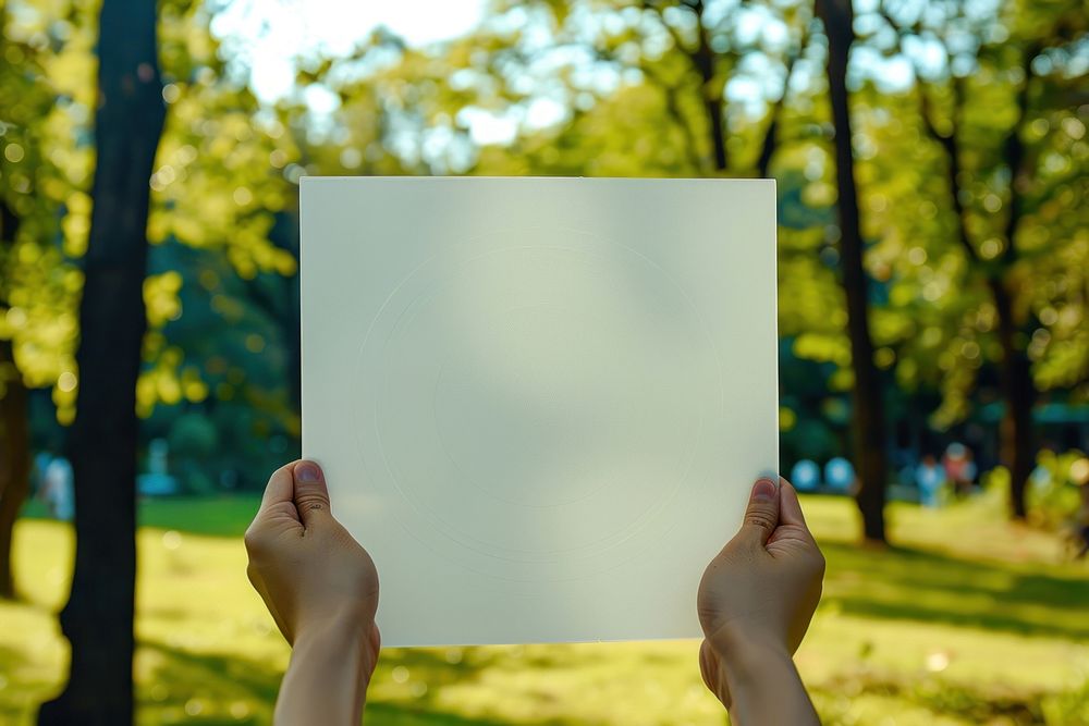 Hand holding blank square paper cover album vinyl record outdoors photo park.