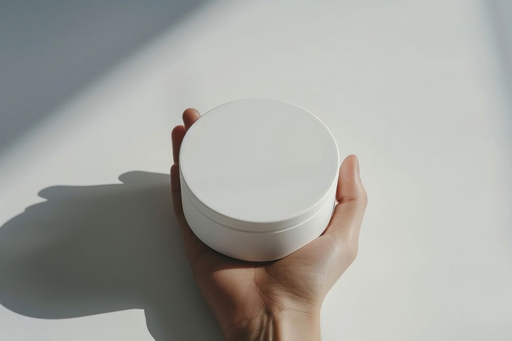 Hand hold white product round shaped box porcelain cosmetics cylinder.