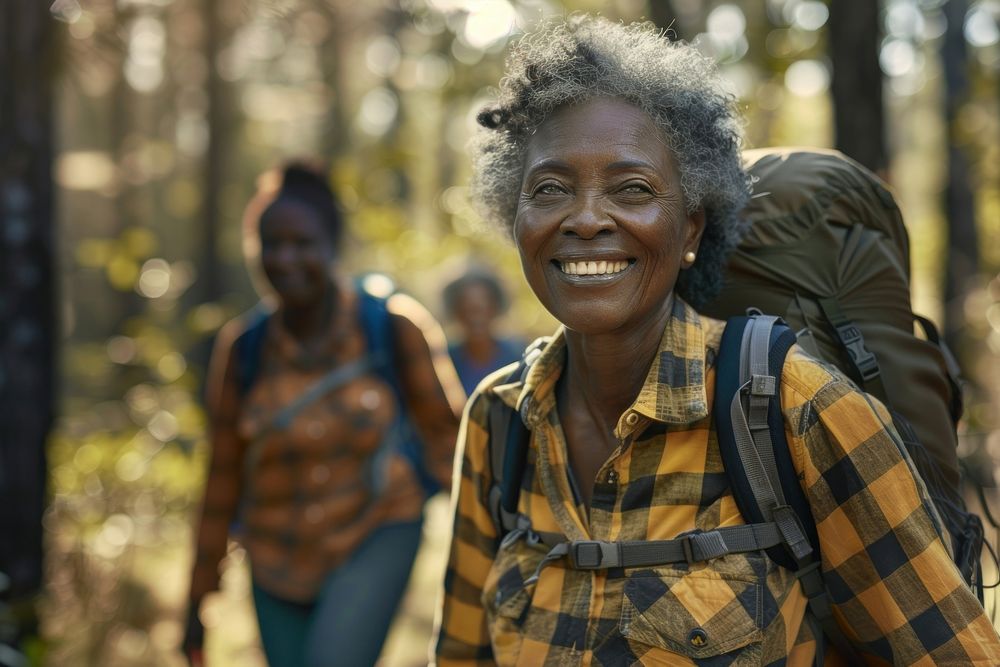 Smiling african senior woman hiking with friends laughing backpack person.