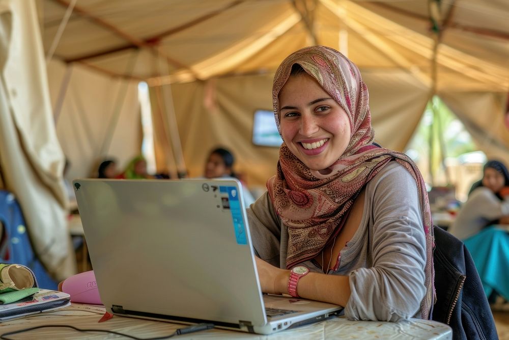 Smiling refugees studying online with laptop in large tents electronics executive computer.